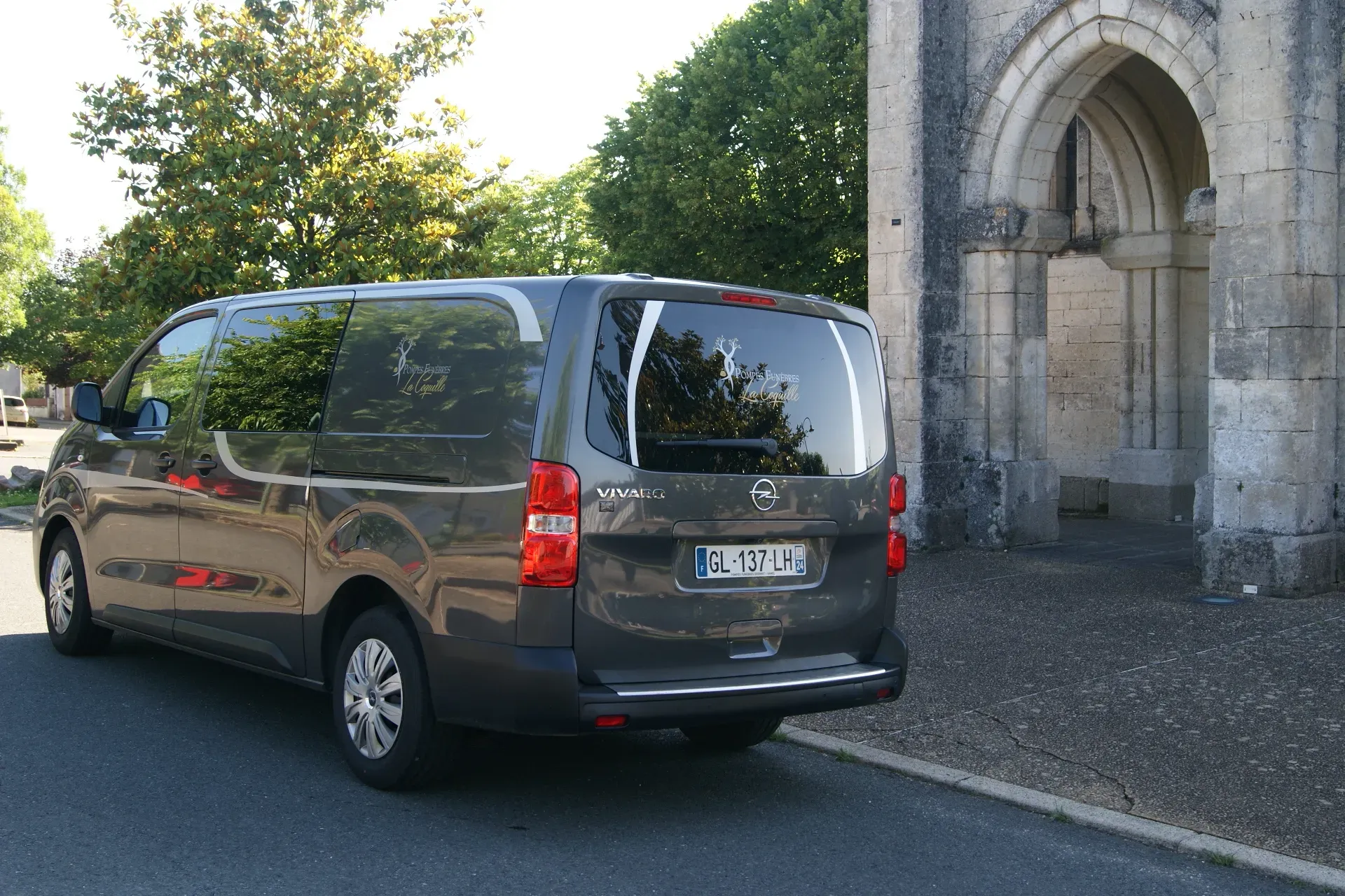 Fourgon funéraire gris stationné devant une église en pierre.